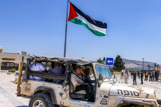 Israeli settlers sit in a four-wheel drive vehicle parked near a group of foreign diplomats accredited by the Palestinian Authority touring during an official visit at the archaeological site of Sebastia, north of Nablus in the occupied West Bank, on June 29, 2026. (Photo by JAAFAR ASHTIYEH / AFP)