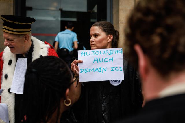 A lawyer holds a placard reading "Today Auch, Tomorrow here" as protesters gather on the steps of the Paris Courthouse while taking part in a "Dead Criminal Justice" day of action called by the council of the Order of the Paris Bar to fight against the "SURE" (Useful, Fast and Effective Sentencing) draft bill, in Paris on June 29, 2026. (Photo by SIMON WOHLFAHRT / AFP)