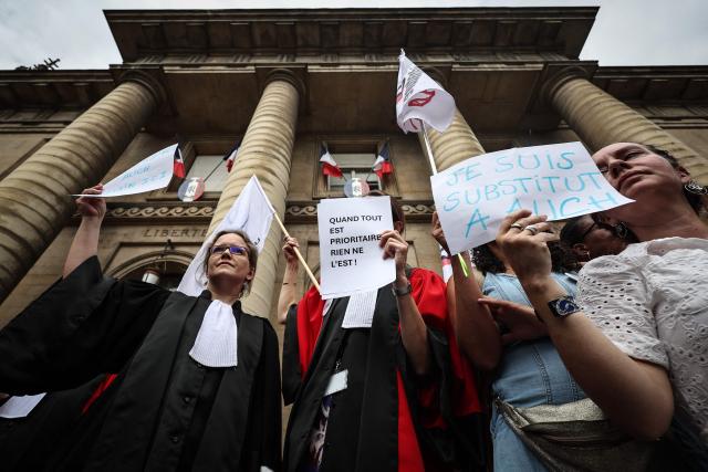A judge (C) holds a placard reading "When everything is priority, nothing is !" as protesters gather on the steps of the Paris Courthouse while taking part in a "Dead Criminal Justice" day of action called by the council of the Order of the Paris Bar to fight against the "SURE" (Useful, Fast and Effective Sentencing) draft bill, in Paris on June 29, 2026. (Photo by SIMON WOHLFAHRT / AFP)