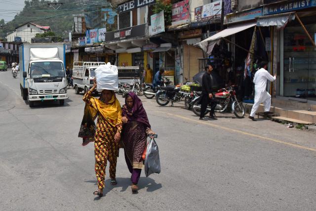 Residents carry groceries as they cross a street at a marketplace after it re-opened in Muzaffarabad, the capital of Pakistan-administered Kashmir on June 29, 2026 following weeks-long protests called by the Joint Awami Action Committee (JAAC) after local authorities banned the group under anti-terrorism laws. A nearly two-week standoff between protesters and police in Pakistan-administered Kashmir has left residents grappling with food shortages, while the death toll from clashes rose to 22, according to an AFP tally on June 17. (Photo by AFP)