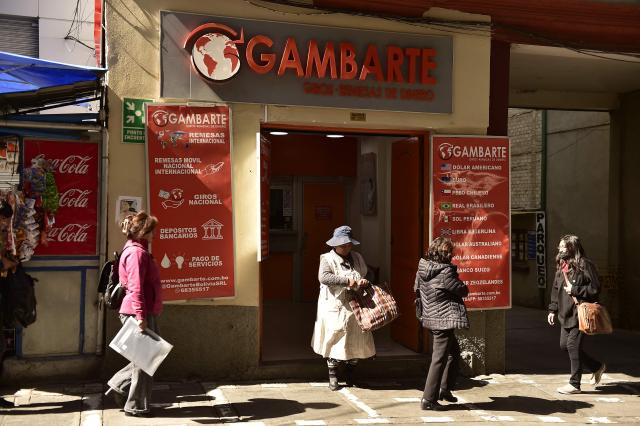 Women walk outside a currency exchange bureau in downtown La Paz on June 29, 2026. Bolivia lifted a 15-year peg on its dollar exchange rate in a bid to attract more greenbacks, a move aimed at ending a severe economic crisis that has sparked unrest. (Photo by Jorge BERNAL / AFP)