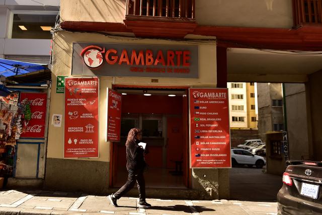 A woman walks past a currency exchange bureau in downtown La Paz on June 29, 2026. Bolivia lifted a 15-year peg on its dollar exchange rate in a bid to attract more greenbacks, a move aimed at ending a severe economic crisis that has sparked unrest. (Photo by Jorge BERNAL / AFP)
