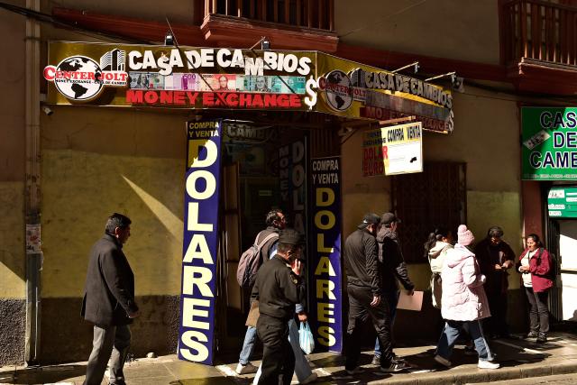 People walk past a currency exchange bureau in downtown La Paz on June 29, 2026. Bolivia lifted a 15-year peg on its dollar exchange rate in a bid to attract more greenbacks, a move aimed at ending a severe economic crisis that has sparked unrest. (Photo by Jorge BERNAL / AFP)