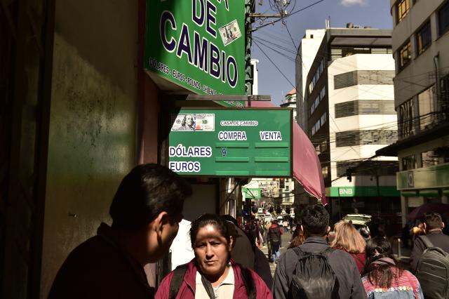 People walk past a currency exchange bureau in downtown La Paz on June 29, 2026. Bolivia lifted a 15-year peg on its dollar exchange rate in a bid to attract more greenbacks, a move aimed at ending a severe economic crisis that has sparked unrest. (Photo by Jorge BERNAL / AFP)