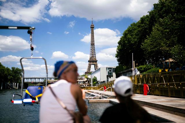 Journalists look at the Seine river at the Baignade de Grenelle Baignade safe swimming site with the Eiffel Tower in the background, in Paris on June 29, 2026. The Baignade de Grenelle Baignade safe swimming will open on July 4, 2026. (Photo by Julie SEBADELHA / AFP)