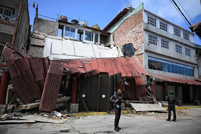 Venezuelan national police officers stand guard outside stores affected by the quakes in El Junquito, Venezuela on June 29, 2026. Hopes were fading on June 29, 2026 of finding survivors more than four days after powerful twin earthquakes struck Venezuela, as residents grow increasingly frustrated with the government's response to the disaster that has killed at least 1,450 people and left tens of thousands unaccounted for. (Photo by Federico PARRA / AFP)