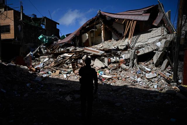 A Venezuelan national police officer of the Criminal Gang Unit stands guard next to rubble in El Junquito, Venezuela on June 29, 2026, after twin earthquakes. Hopes were fading on June 29, 2026 of finding survivors more than four days after powerful twin earthquakes struck Venezuela, as residents grow increasingly frustrated with the government's response to the disaster that has killed at least 1,450 people and left tens of thousands unaccounted for. (Photo by Federico PARRA / AFP)