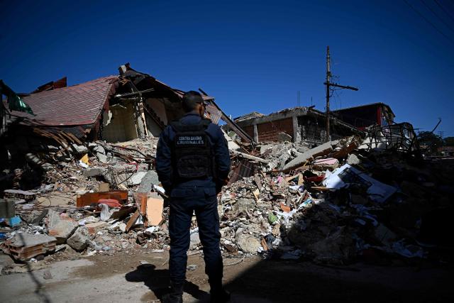 A Venezuelan national police officer of the Criminal Gang Unit stands guard next to rubble in El Junquito, Venezuela on June 29, 2026, after twin earthquakes. Hopes were fading on June 29, 2026 of finding survivors more than four days after powerful twin earthquakes struck Venezuela, as residents grow increasingly frustrated with the government's response to the disaster that has killed at least 1,450 people and left tens of thousands unaccounted for. (Photo by Federico PARRA / AFP)