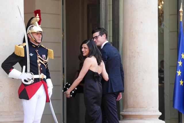 France’s junior Minister in charge of global Francophones and expatriates Eleonore Caroit (C) glances back as she arrives at The Elysee Presidential Palace with her partner Roman Pinosch (R) for a working dinner with France's President and Thailand's King Maha Vajiralongkorn as part of the Thai King's State visit to France, in Paris on June 29, 2026.  (Photo by Dimitar DILKOFF / AFP)