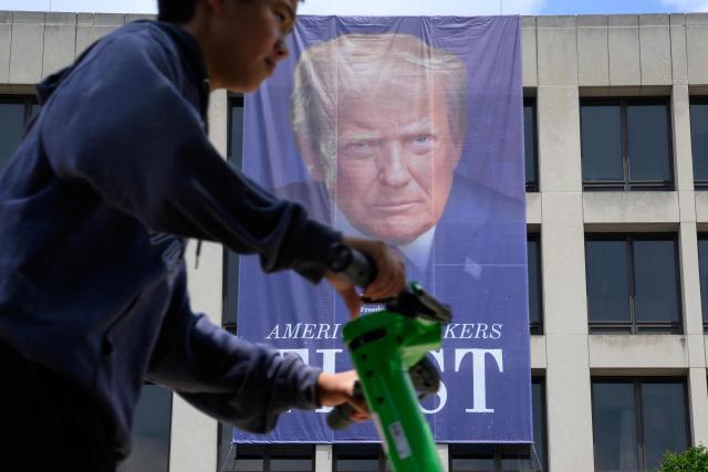 A scooter rider passes by a banner of US President Donald Trump on the side of the US Department of Labor headquarters building in Washington, DC on June 29, 2026. (Photo by Mandel NGAN / AFP)