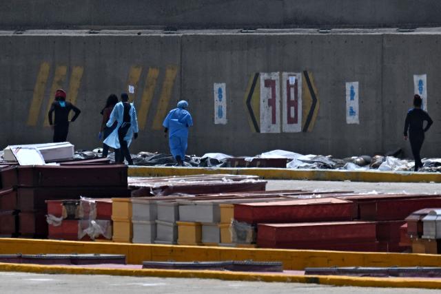 EDITORS NOTE: Graphic content / Forensic experts inspect corpses lined up on the floor near coffins in the port of La Guaira, La Guaira State, Venezuela on June 29, 2026, following the June 24 twin earthquakes. Hopes were fading on June 29, 2026 of finding survivors more than four days after powerful twin earthquakes struck Venezuela, as residents grow increasingly frustrated with the government's response to the disaster that has killed at least 1,450 people and left tens of thousands unaccounted for. (Photo by Juan BARRETO / AFP)