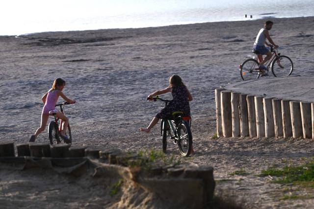 Children ride bikes in the low-water of Lake Velence, close to Gardony city, Hungary on June  29, 2026. The water level has fallen to a historic low, with only 48 centimetres negative recorded on the Agard gauge. Persistent drought, lack of rainfall and extreme evaporation have left increasingly large sections of the shoreline exposed. Temperatures around Lake Velence reached 40–41°C on June  29, 2026, further accelerating the lake’s water loss. (Photo by Attila KISBENEDEK / AFP)
