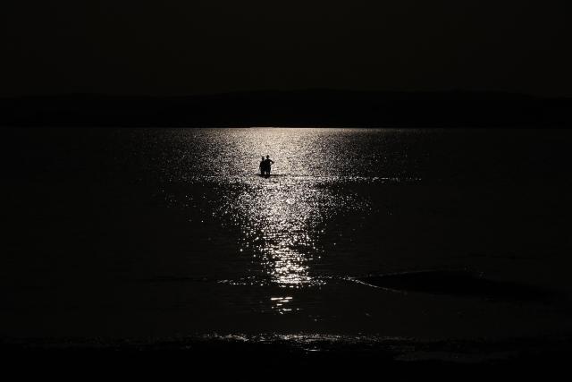 People walk in water of Lake Velence, close to Gardony city, Hungary on June  29, 2026. The water level has fallen to a historic low, with only 48 centimetres negative recorded on the Agard gauge. Persistent drought, lack of rainfall and extreme evaporation have left increasingly large sections of the shoreline exposed. Temperatures around Lake Velence reached 40–41°C on June  29, 2026, further accelerating the lake’s water loss. (Photo by Attila KISBENEDEK / AFP)