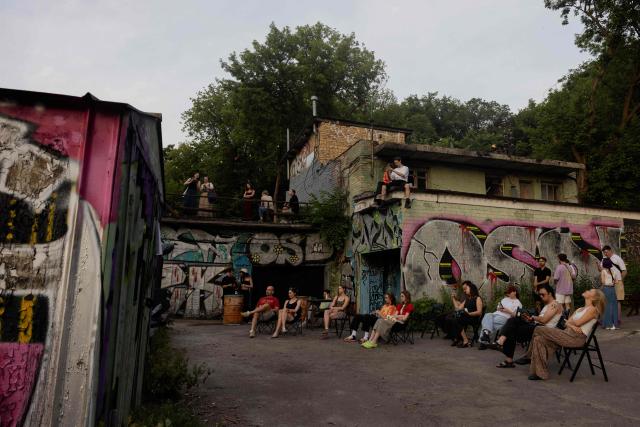 Visitors listen to a concert at the Gak garage art cooperative on a hot evening in Kyiv on June 28, 2026, amid the Russian invasion of Ukraine. Volunteers from 'Repair Together' transformed a site within a garage co-operative into GAK, a cultural space hosting concerts, exhibitions, lectures and community events. 'Repair Together' has been rebuilding villages in Ukraine's Chernihiv region since the area was liberated from Russian forces. (Photo by Tetiana DZHAFAROVA / AFP)