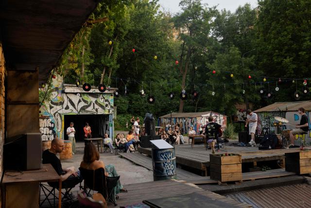 Visitors listen to a concert at the Gak garage art cooperative on a hot evening in Kyiv on June 28, 2026, amid the Russian invasion of Ukraine. Volunteers from 'Repair Together' transformed a site within a garage co-operative into GAK, a cultural space hosting concerts, exhibitions, lectures and community events. 'Repair Together' has been rebuilding villages in Ukraine's Chernihiv region since the area was liberated from Russian forces. (Photo by Tetiana DZHAFAROVA / AFP)
