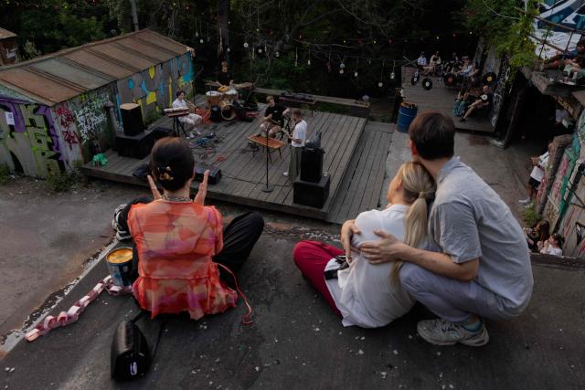 Visitors listen to a concert at the Gak garage art cooperative on a hot evening in Kyiv on June 28, 2026, amid the Russian invasion of Ukraine. Volunteers from 'Repair Together' transformed a site within a garage co-operative into GAK, a cultural space hosting concerts, exhibitions, lectures and community events. 'Repair Together' has been rebuilding villages in Ukraine's Chernihiv region since the area was liberated from Russian forces. (Photo by Tetiana DZHAFAROVA / AFP)