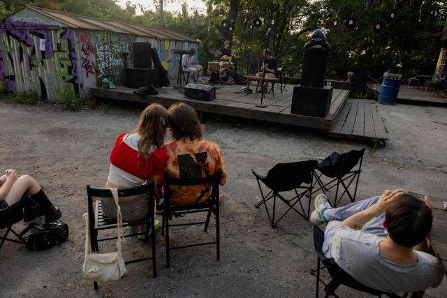 Visitors listen to a concert at the Gak garage art cooperative on a hot evening in Kyiv on June 28, 2026, amid the Russian invasion of Ukraine. Volunteers from 'Repair Together' transformed a site within a garage co-operative into GAK, a cultural space hosting concerts, exhibitions, lectures and community events. 'Repair Together' has been rebuilding villages in Ukraine's Chernihiv region since the area was liberated from Russian forces. (Photo by Tetiana DZHAFAROVA / AFP)
