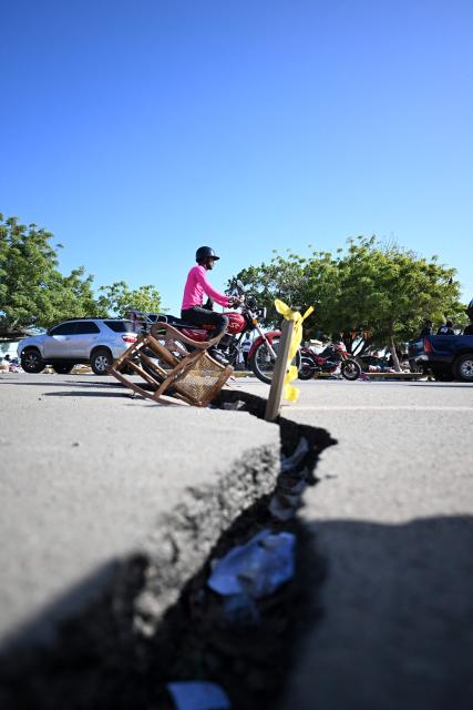 A motorcyclist rides past a large crack in a damaged road in Caraballeda, La Guaira state, Venezuela, on June 29, 2026, following twin earthquakes that struck the country. Devastating back-to-back 7.2 and 7.5 magnitude earthquakes struck near Venezuela's Caribbean coast last week, collapsing buildings, damaging the country's main airport and leaving more than 1,700 people dead and tens of thousands missing. (Photo by Juan BARRETO / AFP)