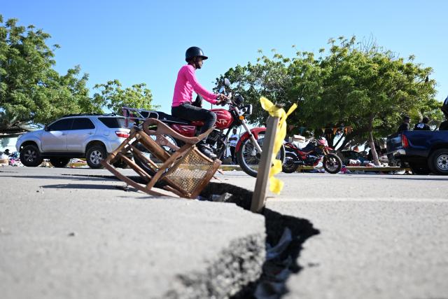 A motorcyclist rides past a large crack in a damaged road in Caraballeda, La Guaira state, Venezuela, on June 29, 2026, following twin earthquakes that struck the country. Devastating back-to-back 7.2 and 7.5 magnitude earthquakes struck near Venezuela's Caribbean coast last week, collapsing buildings, damaging the country's main airport and leaving more than 1,700 people dead and tens of thousands missing. (Photo by Juan BARRETO / AFP)