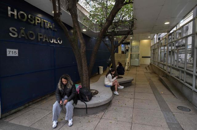 People sit at the entrance to the Sao Paulo Hospital where Brazilian Indigenous leader Chief Raoni Metuktire of the Caiapo people, is hospitalized for medical treatment, in Sao Paulo, Brazil, on June 29, 2026. Last week, Raoni Metuktire, the most recognized face of the fight to save the Amazon rainforest, was moved out of intensive care after intestinal surgery and is recovering "satisfactorily," (Photo by Nelson ALMEIDA / AFP)