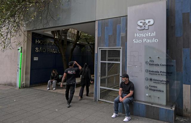 People sit at the entrance to the Sao Paulo Hospital where Brazilian Indigenous leader Chief Raoni Metuktire of the Caiapo people, is hospitalized for medical treatment, in Sao Paulo, Brazil, on June 29, 2026. Last week, Raoni Metuktire, the most recognized face of the fight to save the Amazon rainforest, was moved out of intensive care after intestinal surgery and is recovering "satisfactorily," (Photo by Nelson ALMEIDA / AFP)