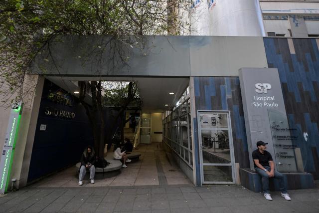 People sit at the entrance to the Sao Paulo Hospital where Brazilian Indigenous leader Chief Raoni Metuktire of the Caiapo people, is hospitalized for medical treatment, in Sao Paulo, Brazil, on June 29, 2026. Last week, Raoni Metuktire, the most recognized face of the fight to save the Amazon rainforest, was moved out of intensive care after intestinal surgery and is recovering "satisfactorily," (Photo by Nelson ALMEIDA / AFP)