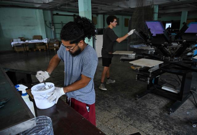 Men work at the private screen-printing business La Cabra Studio in Havana on June 22, 2026. Food, transport and even fuel imports: the private sector, once marginal, is now establishing itself in a Cuba in crisis and is set to grow further following the recent liberalisation measures approved by the government. (Photo by YAMIL LAGE / AFP)