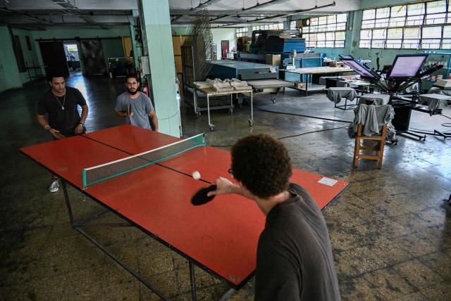 Employees play table tennis while waiting for electricity to be restored at La Cabra Studio, a private screen-printing studio, in Havana on June 22, 2026. Food, transport and even fuel imports: the private sector, once marginal, is now establishing itself in a Cuba in crisis and is set to grow further following the recent liberalisation measures approved by the government. (Photo by YAMIL LAGE / AFP)