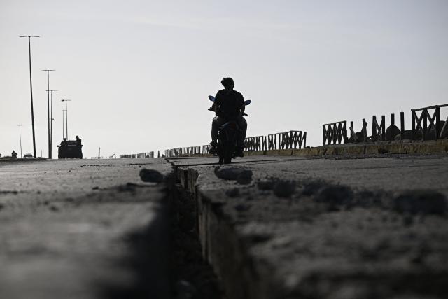 A motorcyclist rides past a cracked roadway along a coastal road in the Playa Verde sector of Catia La Mar, La Guaira state, Venezuela, on June 29, 2026, following twin earthquakes. Hopes were fading of finding survivors more than four days after powerful twin earthquakes struck Venezuela, as residents grow increasingly frustrated with the government's response to the disaster that has killed -up to now- more than 1,700 people and left tens of thousands unaccounted for. (Photo by Federico PARRA / POOL / AFP)