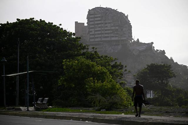 A man walks along a roadside with a heavily damaged multi-storey building in the background in the Playa Verde sector of Catia La Mar, La Guaira state, Venezuela, on June 29, 2026, following twin earthquakes. Hopes were fading of finding survivors more than four days after powerful twin earthquakes struck Venezuela, as residents grow increasingly frustrated with the government's response to the disaster that has killed -up to now- more than 1,700 people and left tens of thousands unaccounted for. (Photo by Federico PARRA / POOL / AFP)