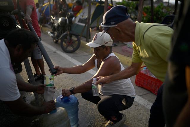 Residents fill water containers from a pipe along a roadside in the Playa Verde sector of Catia La Mar, La Guaira state, Venezuela, on June 29, 2026, following twin earthquakes. Hopes were fading of finding survivors more than four days after powerful twin earthquakes struck Venezuela, as residents grow increasingly frustrated with the government's response to the disaster that has killed -up to now- more than 1,700 people and left tens of thousands unaccounted for. (Photo by Federico PARRA / POOL / AFP)