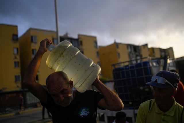 A resident carries a large container of water near damaged apartment buildings in the Playa Verde sector of Catia La Mar, La Guaira state, Venezuela, on June 29, 2026, following twin earthquakes. Hopes were fading of finding survivors more than four days after powerful twin earthquakes struck Venezuela, as residents grow increasingly frustrated with the government's response to the disaster that has killed -up to now- more than 1,700 people and left tens of thousands unaccounted for. (Photo by Federico PARRA / POOL / AFP)