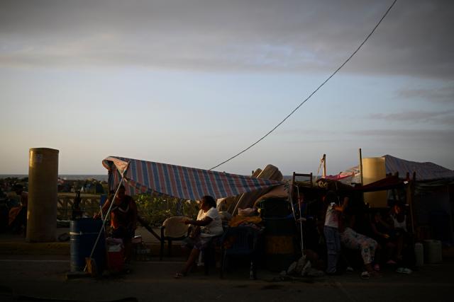 Displaced residents gather under makeshift tarpaulin shelters set up along a roadside in the Playa Verde sector of Catia La Mar, La Guaira state, Venezuela, on June 29, 2026, following twin earthquakes. Hopes were fading of finding survivors more than four days after powerful twin earthquakes struck Venezuela, as residents grow increasingly frustrated with the government's response to the disaster that has killed -up to now- more than 1,700 people and left tens of thousands unaccounted for. (Photo by Federico PARRA / POOL / AFP)