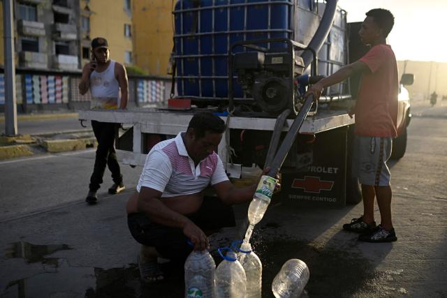 Residents fill plastic containers with water from a tanker truck in the Playa Verde sector of Catia La Mar, La Guaira state, Venezuela, on June 29, 2026, following twin earthquakes. Hopes were fading of finding survivors more than four days after powerful twin earthquakes struck Venezuela, as residents grow increasingly frustrated with the government's response to the disaster that has killed -up to now- more than 1,700 people and left tens of thousands unaccounted for. (Photo by Federico PARRA / POOL / AFP)