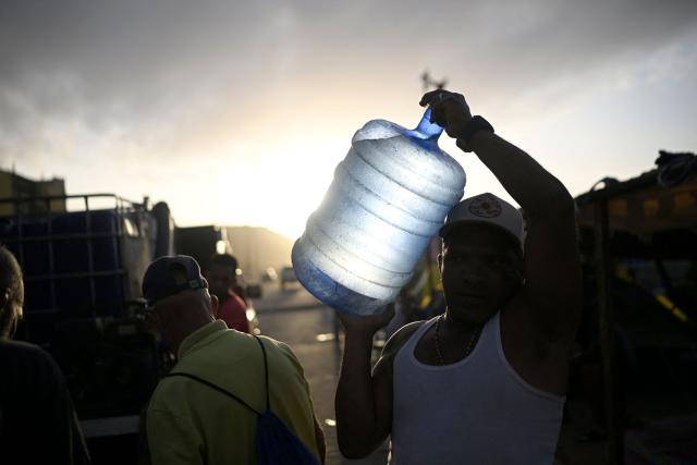 A resident carries a large container of water near damaged apartment buildings in the Playa Verde sector of Catia La Mar, La Guaira state, Venezuela, on June 29, 2026, following twin earthquakes. Hopes were fading of finding survivors more than four days after powerful twin earthquakes struck Venezuela, as residents grow increasingly frustrated with the government's response to the disaster that has killed -up to now- more than 1,700 people and left tens of thousands unaccounted for. (Photo by Federico PARRA / POOL / AFP)