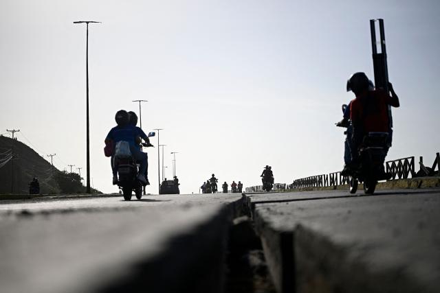 Motorcyclists ride past a cracked roadway along a coastal road in the Playa Verde sector of Catia La Mar, La Guaira state, Venezuela, on June 29, 2026, following twin earthquakes. Hopes were fading of finding survivors more than four days after powerful twin earthquakes struck Venezuela, as residents grow increasingly frustrated with the government's response to the disaster that has killed -up to now- more than 1,700 people and left tens of thousands unaccounted for. (Photo by Federico PARRA / POOL / AFP)