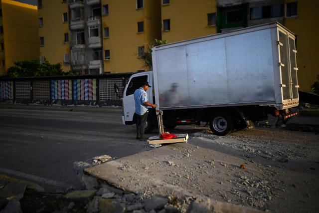 A man stands next to a truck passing by a damaged roadside amid debris near apartment buildings in the Playa Verde sector of Catia La Mar, La Guaira state, Venezuela, on June 29, 2026, following twin earthquakes. Hopes were fading of finding survivors more than four days after powerful twin earthquakes struck Venezuela, as residents grow increasingly frustrated with the government's response to the disaster that has killed -up to now- more than 1,700 people and left tens of thousands unaccounted for. (Photo by Federico PARRA / POOL / AFP)