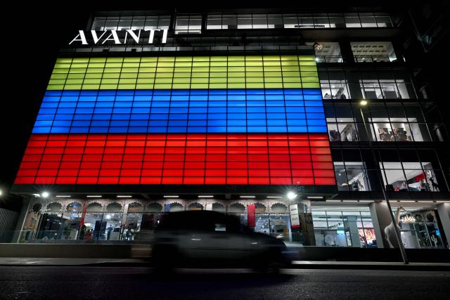 The facade of a retail store is illuminated in the colors of the Venezuelan flag in Caracas, on June 29, 2026. Hopes were fading of finding survivors more than four days after powerful twin earthquakes struck Venezuela, as residents grow increasingly frustrated with the government's response to the disaster that has killed -up to now- more than 1,700 people and left tens of thousands unaccounted for. (Photo by Juan BARRETO / AFP)