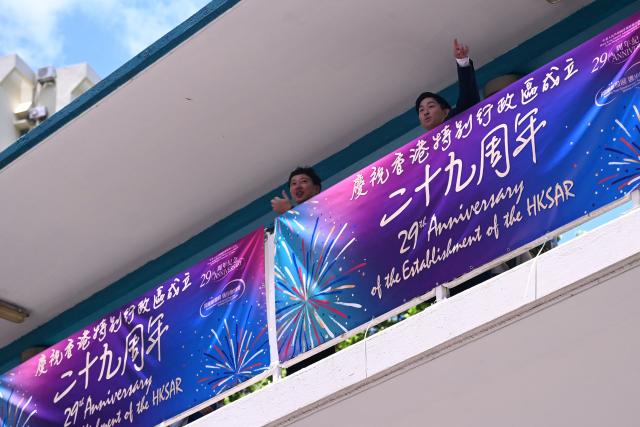 People look out over a banner marking the 29th anniversary of the handover of Hong Kong from Britain to China in Hong Kong on June 30, 2026. (Photo by Peter PARKS / AFP)