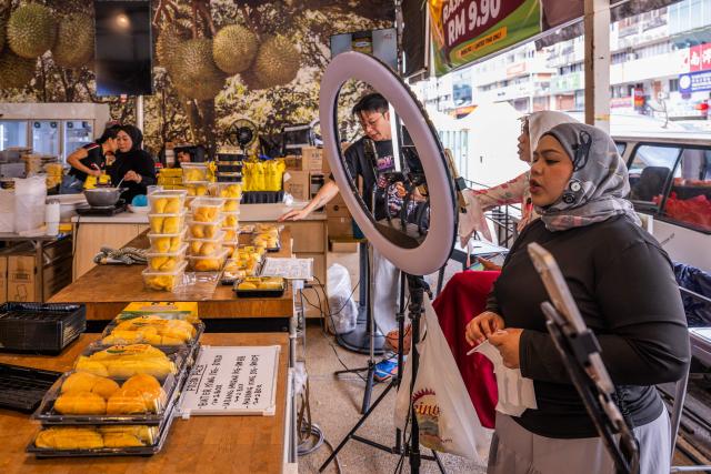 This photo taken on June 29, 2026 shows live streamers selling durians through an online livestream at a durian shop in Kuala Lumpur. Found across Southeast Asia, the spiky fruit comes in many varieties and in Malaysia, the highly prized cultivar Musang King is consumed locally and exported, mainly to China. Malaysia, which produces more than 550,000 tonnes of durian a year, is currently in its peak harvest season. (Photo by Mohd Rasfan / AFP)