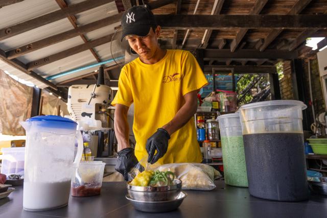 This photo taken on June 27, 2026 shows a worker preparing a Musang King durian cendol dessert for customers in Karak, in Malaysia's Pahang state. Found across Southeast Asia, the spiky fruit comes in many varieties and in Malaysia, the highly prized cultivar Musang King is consumed locally and exported, mainly to China. Malaysia, which produces more than 550,000 tonnes of durian a year, is currently in its peak harvest season. (Photo by Mohd Rasfan / AFP)