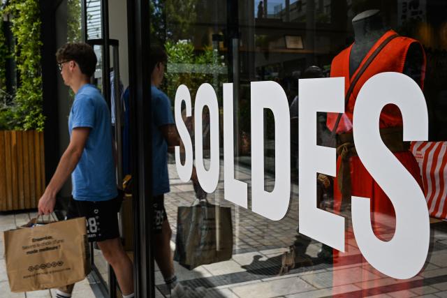 (FILES) A customer walks past the entrance of a department store bearing a placard promoting French summer sales on the opening day in Beziers, Southern France, on June 24, 2026. The summer sales period, which was originally scheduled to end on July 21, has been extended by one week, until July 28, to compensate for low foot traffic in stores during the heat wave, Commerce Minister announced on June 30, 2026. (Photo by Gabriel BOUYS / AFP)