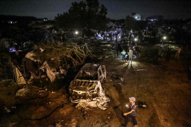 Palestinians stand next to the wreckage of a car and destroyed shelters at the site of an Israeli strike that was reportedly preceded by an Israeli military evacuation warning, at the al-Mawassi camp in Khan Yunis, southern Gaza Strip, late on June 29, 2026. Gaza remains gripped by daily violence, with both the Israeli military and Hamas accusing one another of violating the truce in effect since October 10. (Photo by Bashar Taleb / AFP)