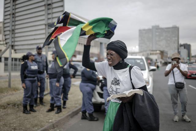 A woman holds a South African flag as she prays in front of members of the South African Police Service (SAPS) ahead of planned demonstrations by the March and March movement against the presence of undocumented migrants in South Africa, in Durban, on June 30, 2026. South African police deployed to head off unrest and protests on June 30, 2026, the unofficial deadline set by citizen-led groups for undocumented foreign nationals to leave that has already pushed thousands to flee.
Officers were out in force to prevent violence and looting, while hundreds of foreign nationals took refuge in several cities, urgently seeking help to leave. (Photo by Rajesh JANTILAL / AFP)