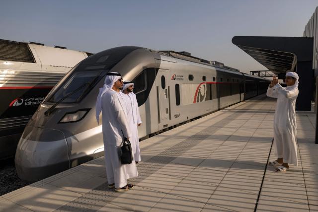 Men pose for a photograph in front of an Etihad Rail train, the UAE's first passenger train, on its inaugural journey at Mohamed bin Zayed City station in Abu Dhabi on June 30, 2026. The passenger service will eventually connect four of the country's seven emirates, with an "introductory operational phase" between Abu Dhabi and Fujairah to begin on June 30, state news agency WAM said earlier this month. The Dubai station will open on September 30, while the main station in the neighbouring emirate of Sharjah is set to be operational on March 30, 2027. (Photo by FADEL SENNA / AFP)