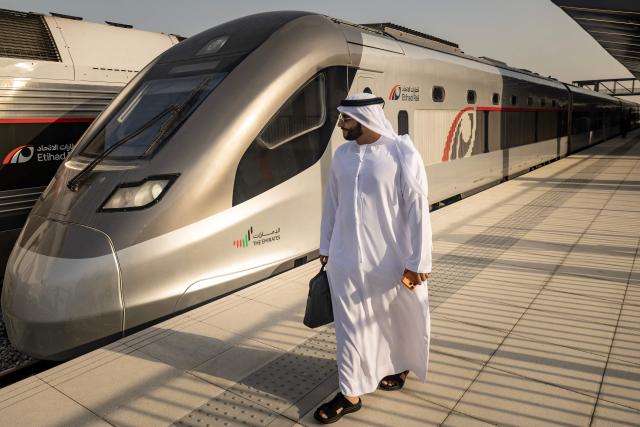 A man stands next to an Etihad Rail train, the UAE's first passenger train, on its inaugural journey at Mohamed bin Zayed City station in Abu Dhabi on June 30, 2026. The passenger service will eventually connect four of the country's seven emirates, with an "introductory operational phase" between Abu Dhabi and Fujairah to begin on June 30, state news agency WAM said earlier this month. The Dubai station will open on September 30, while the main station in the neighbouring emirate of Sharjah is set to be operational on March 30, 2027. (Photo by FADEL SENNA / AFP)