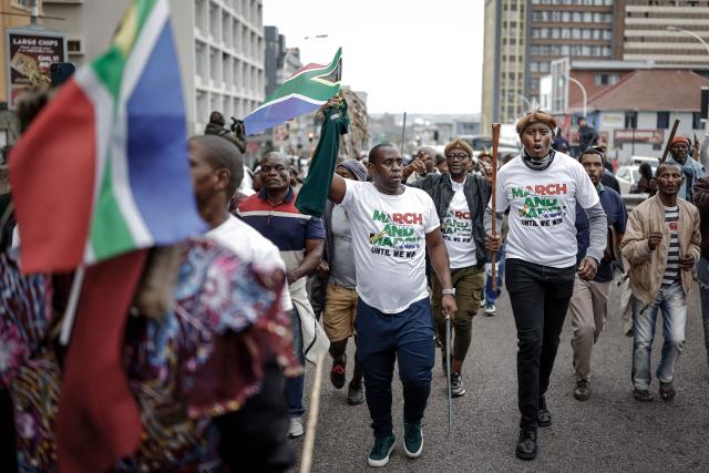 Protesters hold flags and chant slogans as they march during a demonstration by the "March and March" movement marking an unofficial deadline set by citizen-led groups for undocumented foreign nationals to leave South Africa, in Durban, on June 30, 2026. South African police deployed to head off unrest and protests on June 30, 2026, the unofficial deadline set by anti-immigrant groups for undocumented foreign nationals to leave that has already pushed thousands to flee.
Officers were out in force to prevent violence and looting by the xenophobic groups, while hundreds of foreign nationals took refuge in several cities, urgently seeking help to leave. (Photo by Marco LONGARI / AFP)