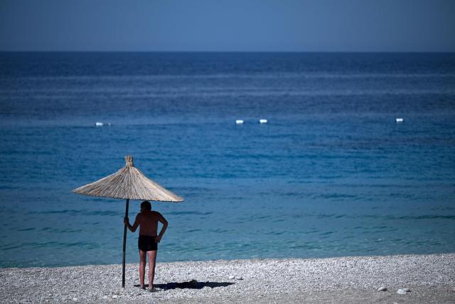 A beach goer stands under the shade of an umbrella on the beach of Dhermi, south of Albania on June 30, 2026. Europe's most severe heatwave on record set new temperature records in eastern parts of the continent on June 29, 2026. (Photo by Armend NIMANI / AFP)