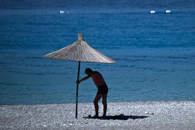 A beach goer stands under the shade of an umbrella on the beach of Dhermi, south of Albania on June 30, 2026. Europe's most severe heatwave on record set new temperature records in eastern parts of the continent on June 29, 2026. (Photo by Armend NIMANI / AFP)
