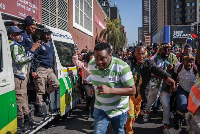 Tshwane Metro Police officers watch from their vehicle as protesters run and chant slogans during a demonstration a demonstration by the "March and March" and Operation Dudula movements marking an unofficial deadline set by citizen-led groups for undocumented foreign nationals to leave South Africa, in downtown Pretoria, on June 30, 2026. South African police deployed to head off unrest and protests on June 30, 2026, the unofficial deadline set by anti-immigrant groups for undocumented foreign nationals to leave that has already pushed thousands to flee.
Officers were out in force to prevent violence and looting by the xenophobic groups, while hundreds of foreign nationals took refuge in several cities, urgently seeking help to leave. (Photo by PHILL MAGAKOE / AFP)